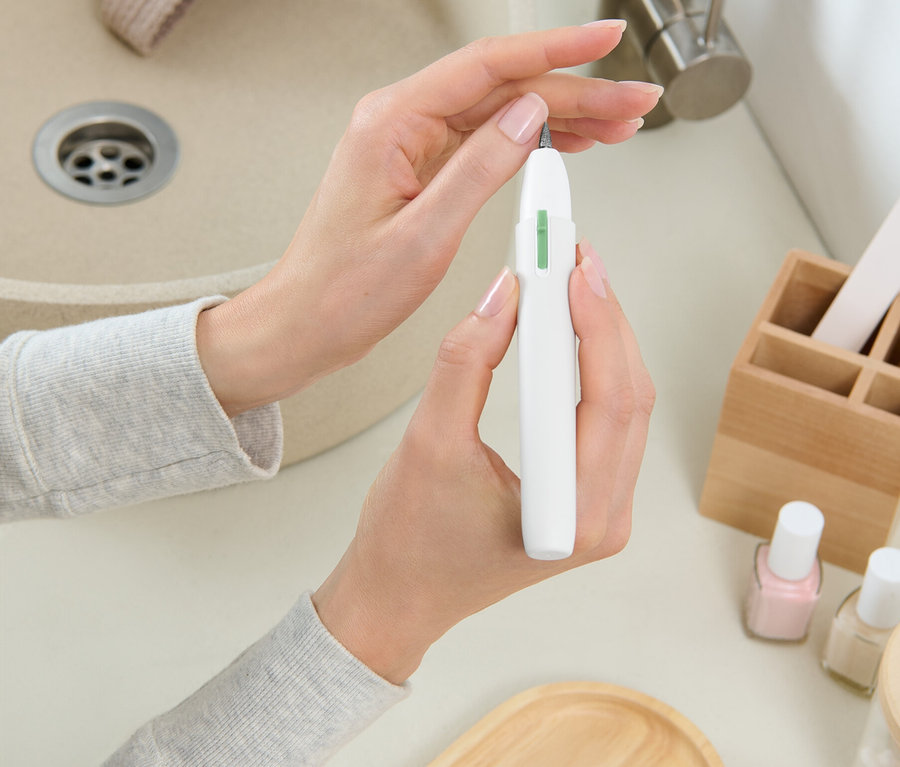 Bir kadın lavabonun önünde beyaz bir tırnak frezesi tutuyor.