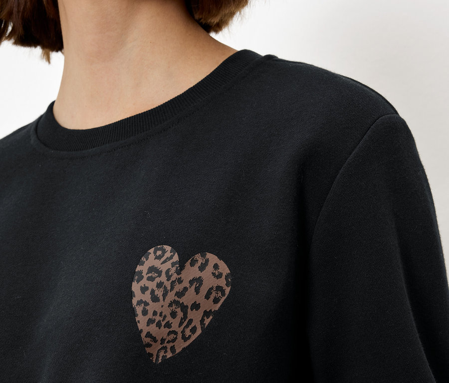 Kadın leopar desenli kalpli siyah bir sweatshirt giyiyor.