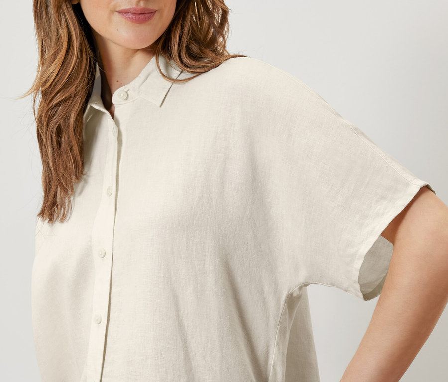 Kadın krem beyazı keten bir bluz giyiyor.