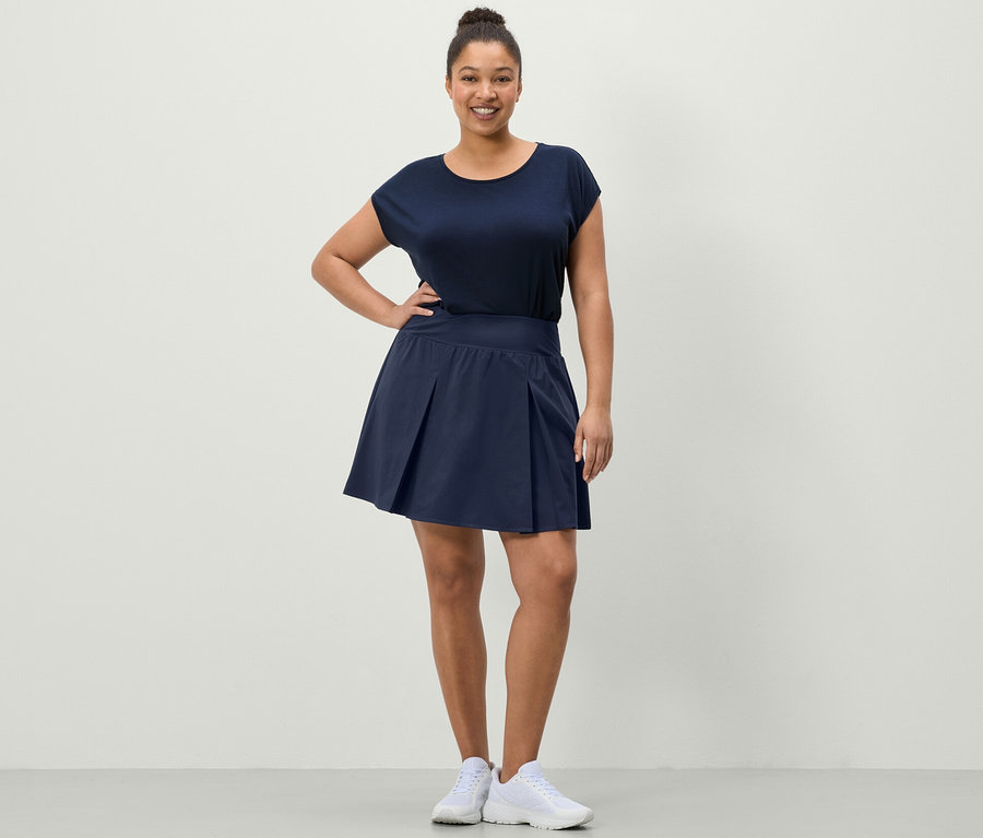 Kadın lacivert spor etek ve mavi spor tişörtü ile poz veriyor.