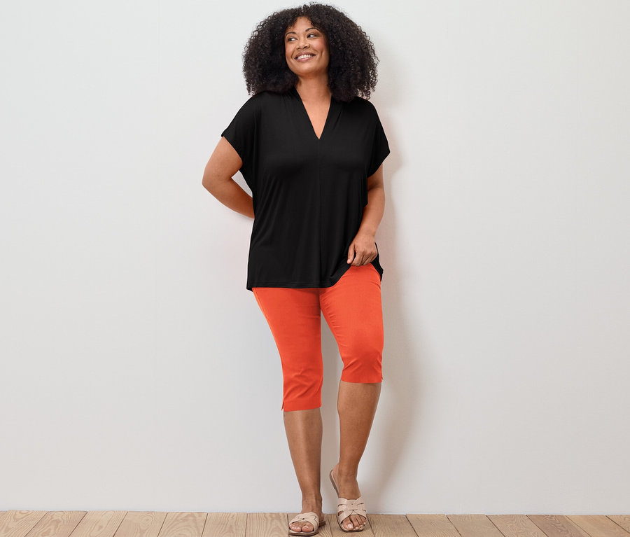 Kadın siyah V yakalı bluz ve turuncu 3/4 streç pantolonla poz veriyor.