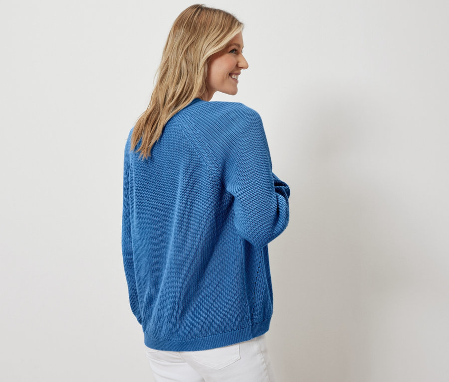 Kadın açık hırka ve beyaz kot pantolonla poz veriyor.