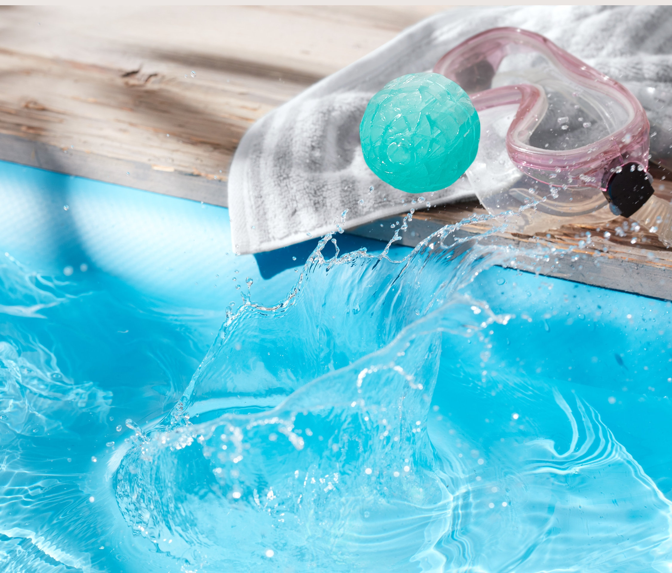 Zıplayan su topu, havuz kenarında bir havlu üzerinde gözlüğün yanında duruyor.