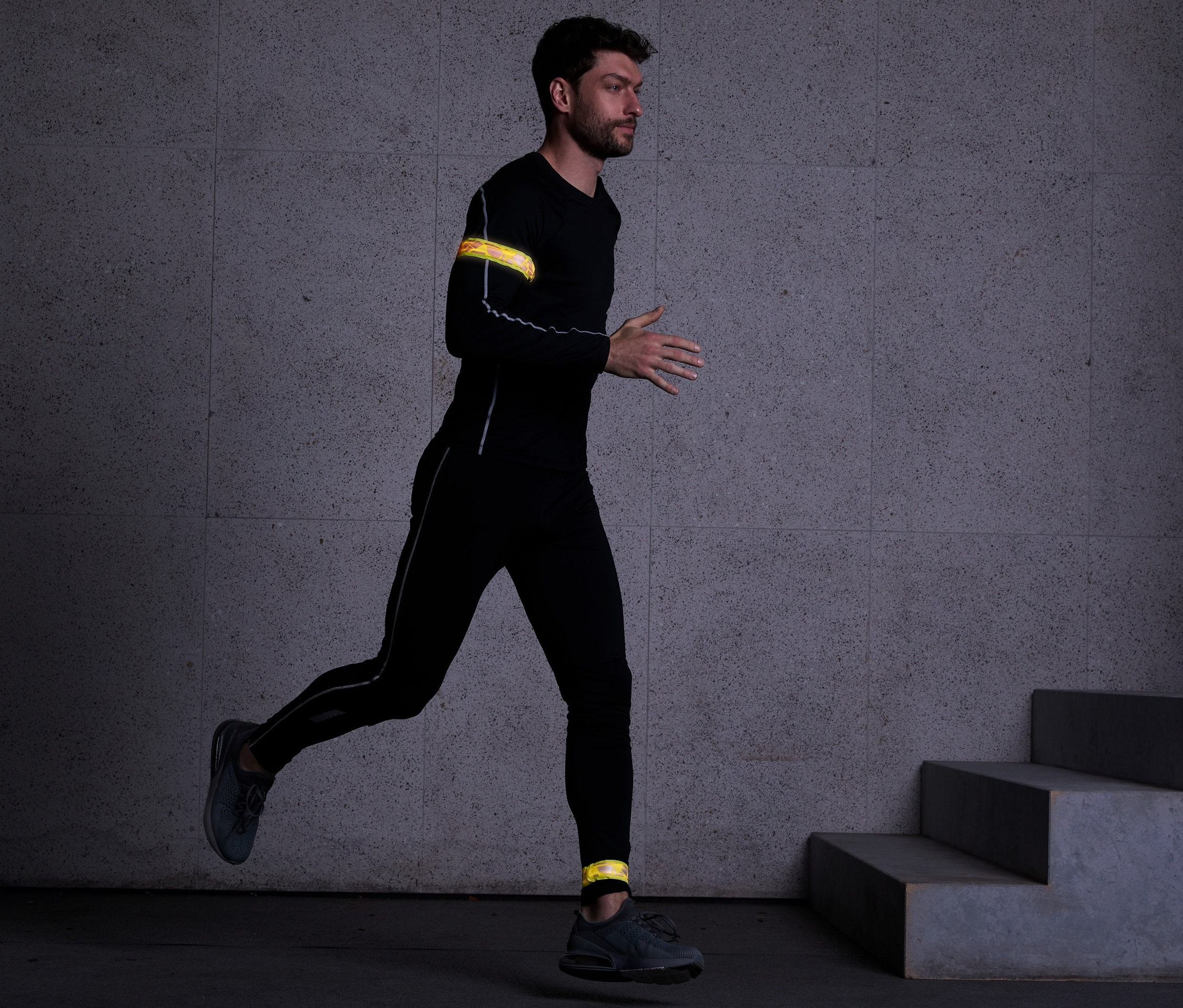 Siyah spor giysili bir adam koşuyor, kolunda ve ayak bileğinde 2 Adet USB'li LED Bileklik var.