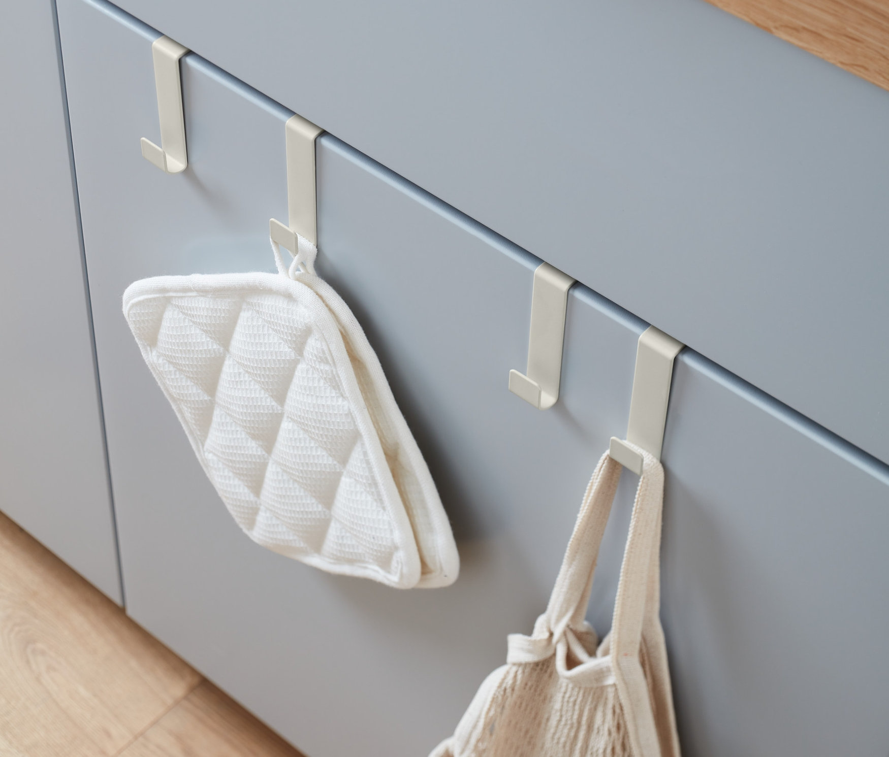 Gri mutfak dolabı kapaklarında 4 adet Kapı Askısı, üzerinde bir tutacak ve bir file çanta asılı duruyor.