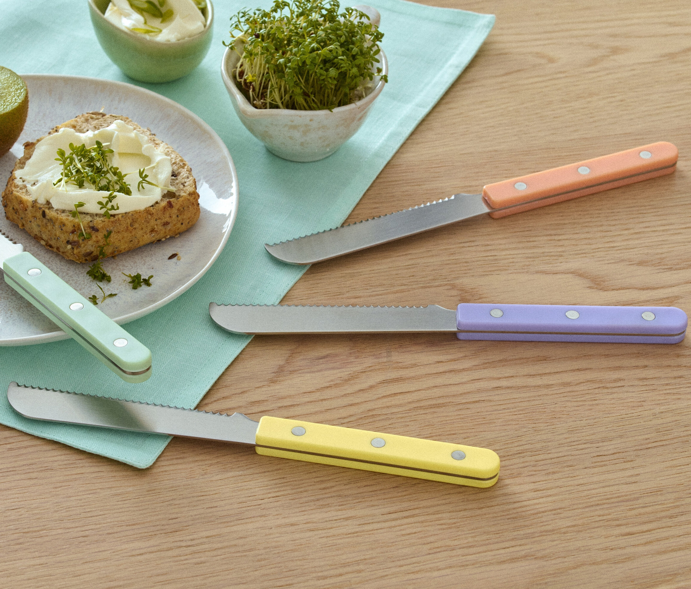 Kivi, sürülebilir ezmeli ekmek ve tere içeren tabağın yanında 4 adet kahvaltı bıçağı.