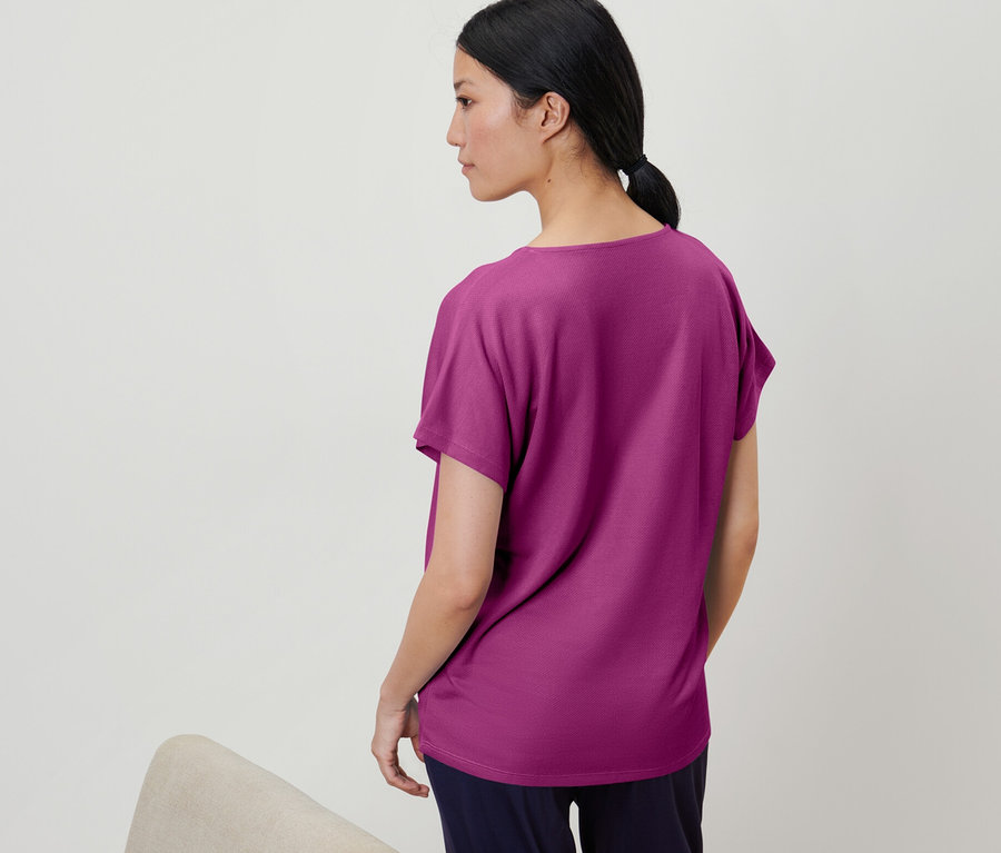 Kadın dokulu ahududu rengi bir tişört giyiyor.