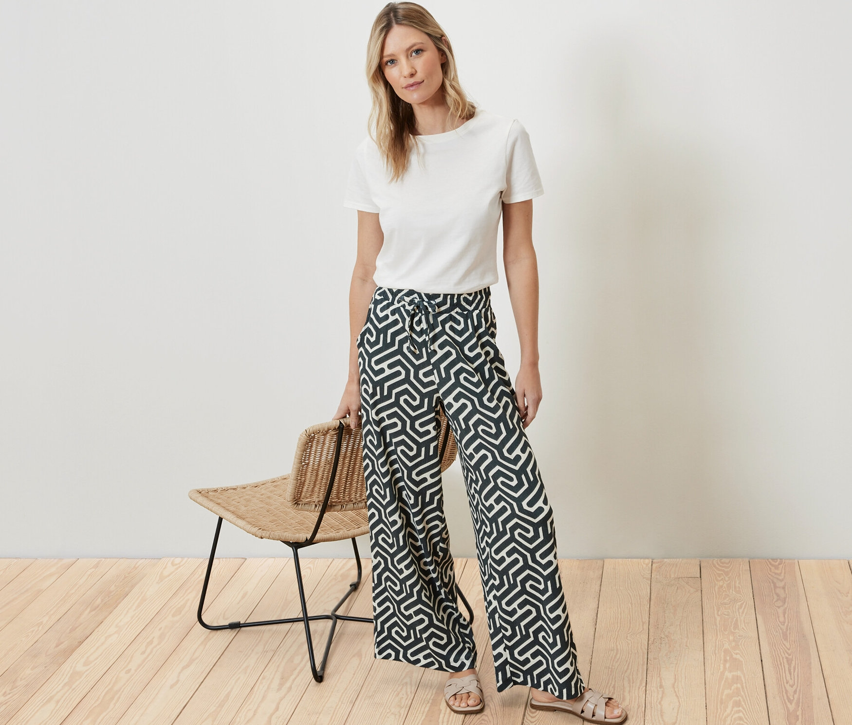 Bir kadın ayakta duruyor, üzerinde beyaz bir tişört ve kırışık görünümlü, baskılı, lastikli bir pantolon var.