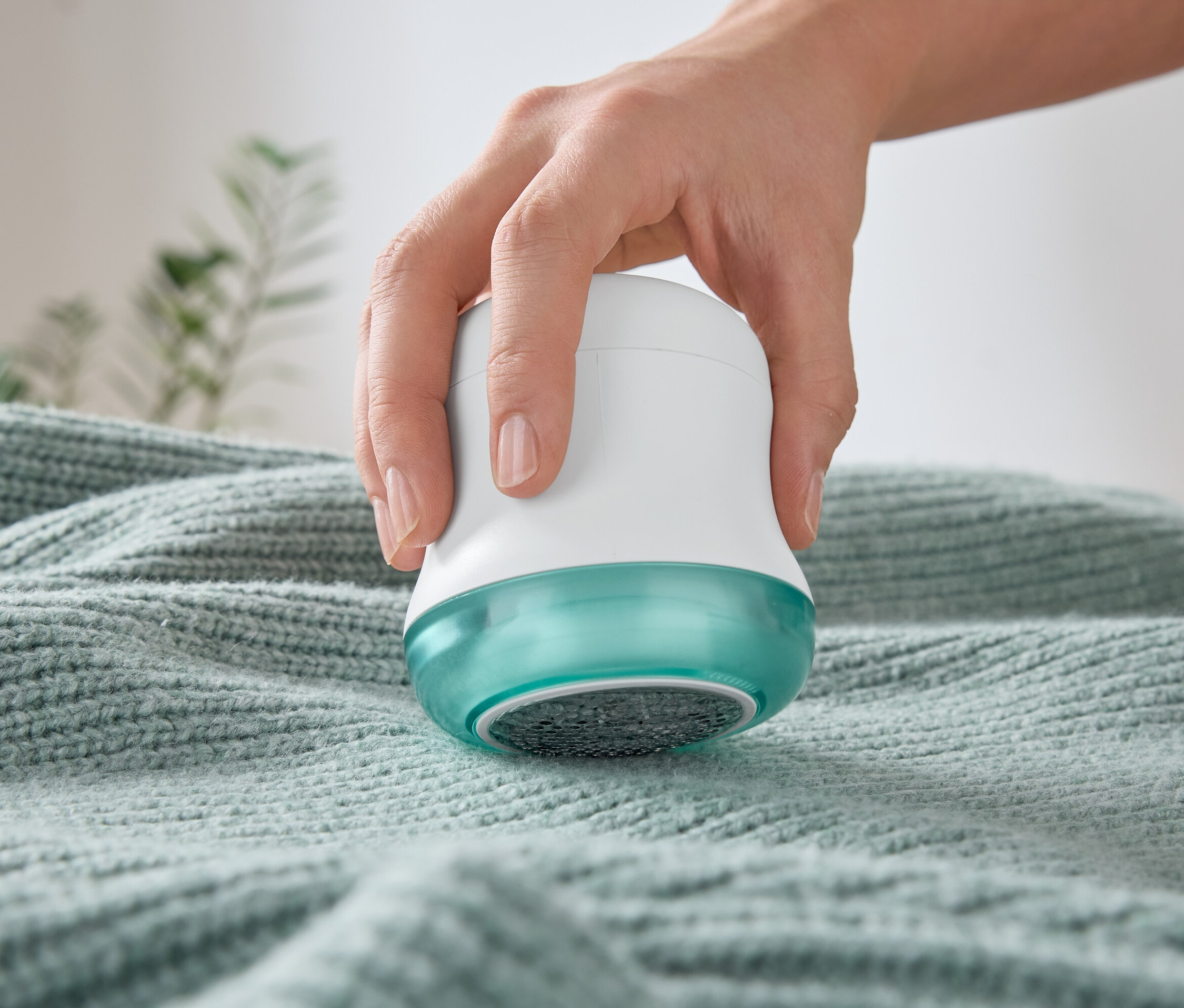 Bir el, bir kazağın üzerinde tüy toplayıcı kullanıyor.