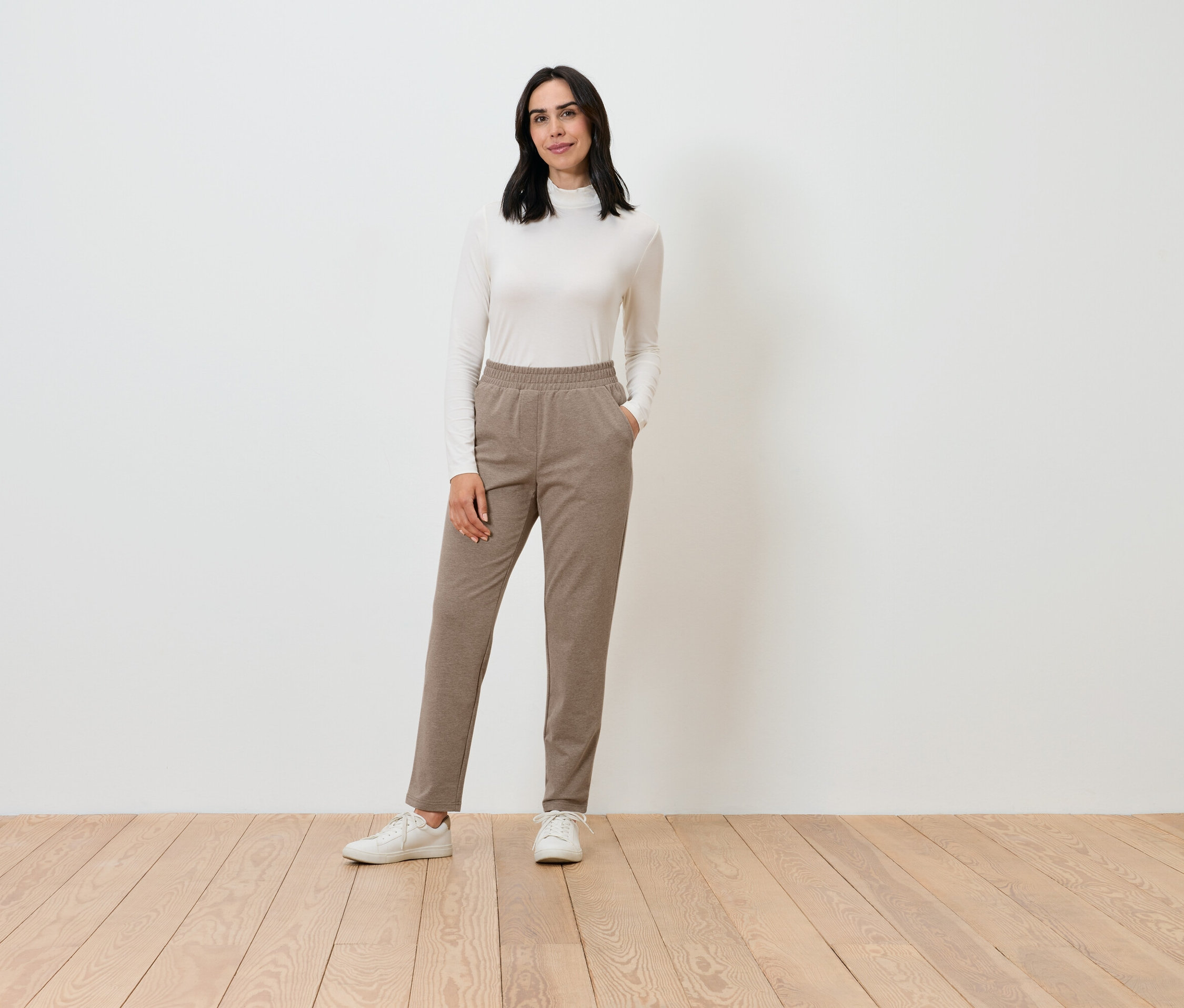 Krem rengi balıkçı yaka ve kahverengi pantolon giyen bir kadın poz veriyor.