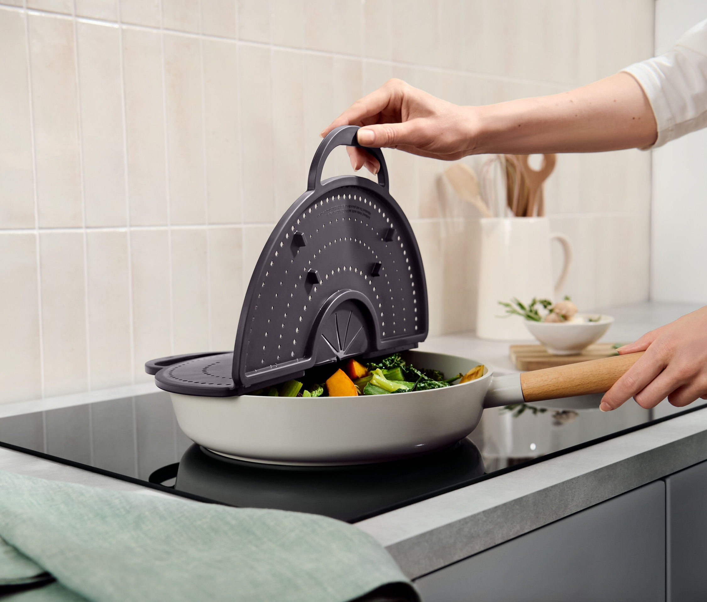 Bir el sebzelerle dolu bir tavanın üzerinde gri bir süzgeç tutuyor.