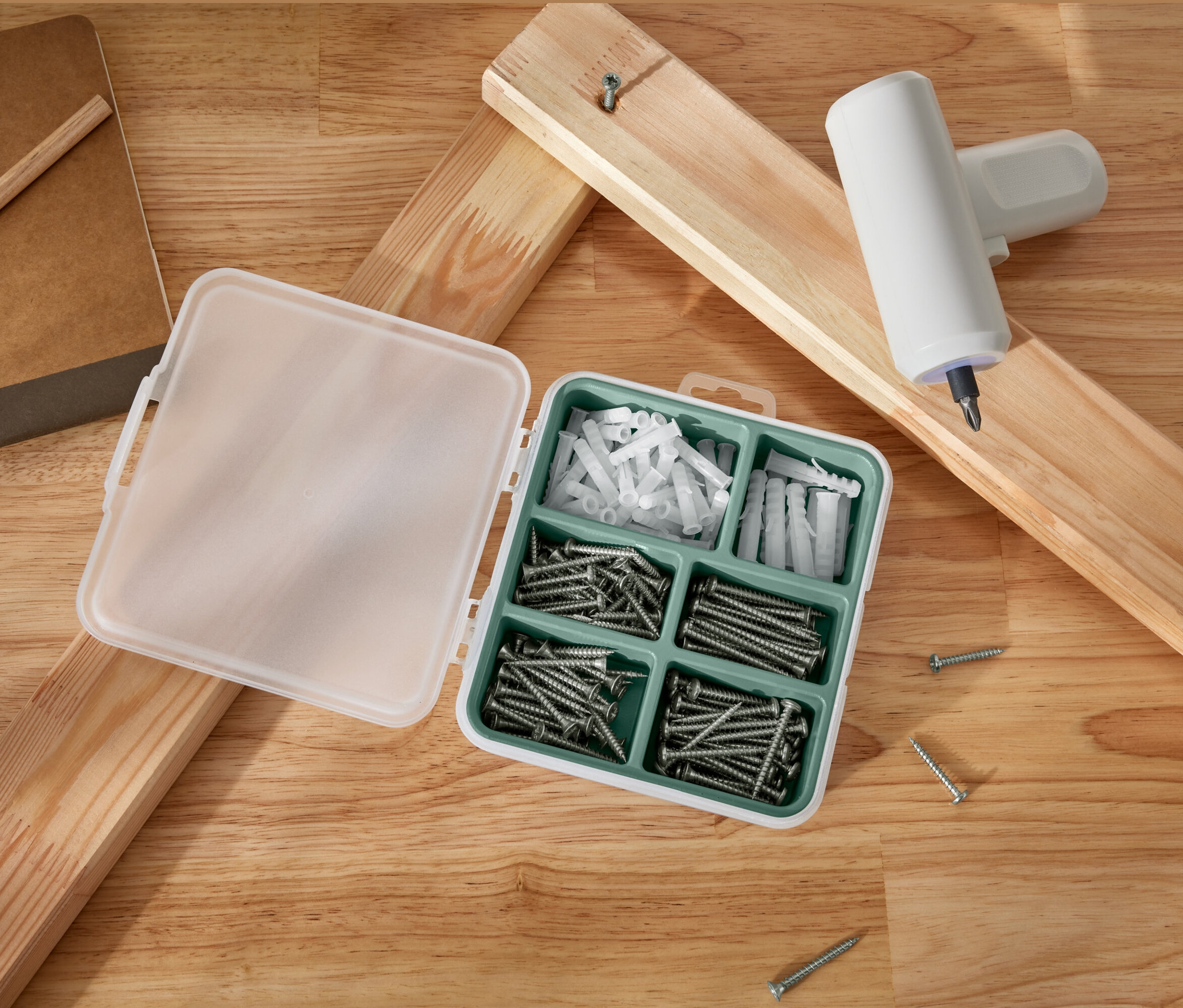 Açık bir vida ve dübel seti, ahşap tahtaların ve akülü bir tornavidanın yanında duruyor.