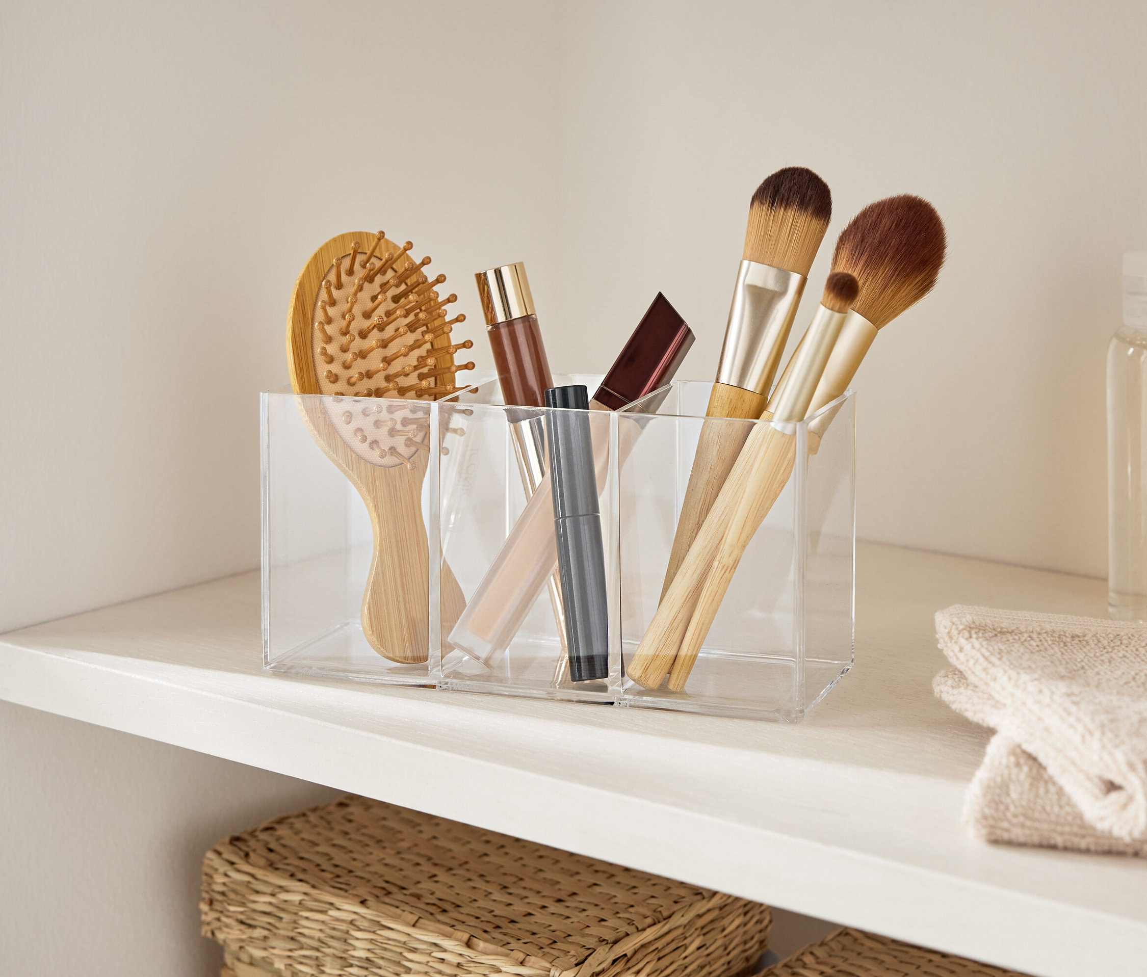 Beyaz bir rafta şeffaf akrilik bir düzenleyicide bulunan bir saç fırçası ve makyaj fırçaları.