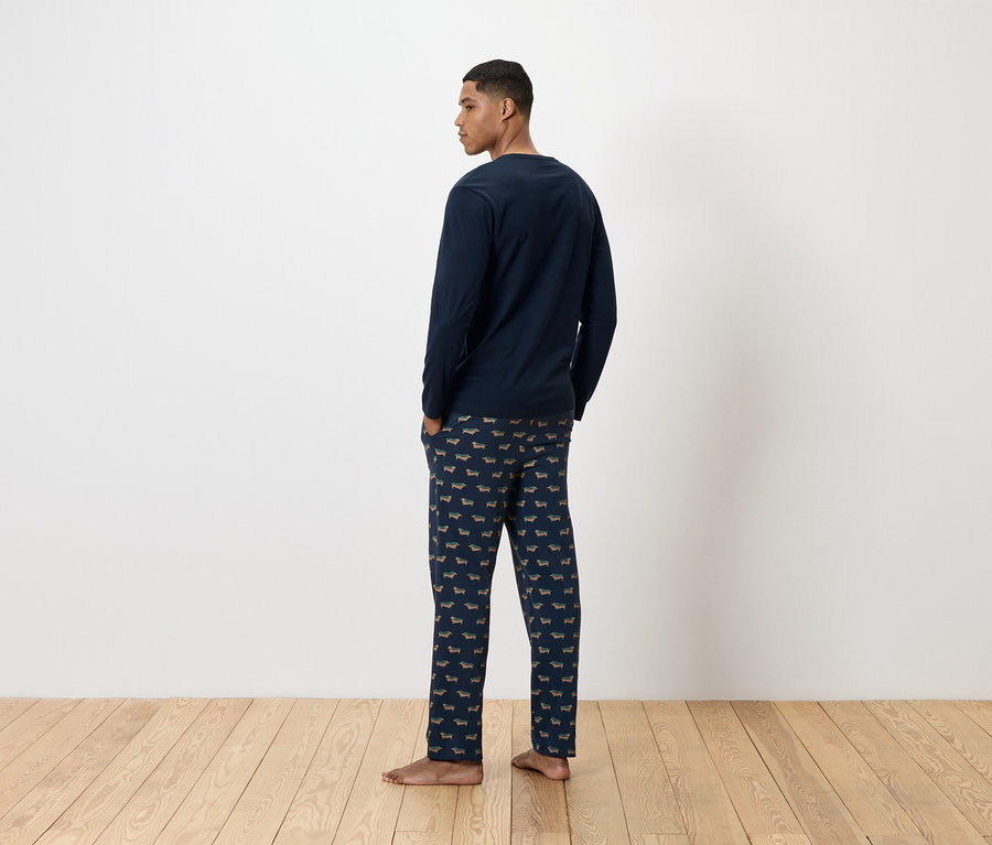 Arkadan görünen bir adam, üzerinde dachshund baskılı lacivert bir pijama takımı var.