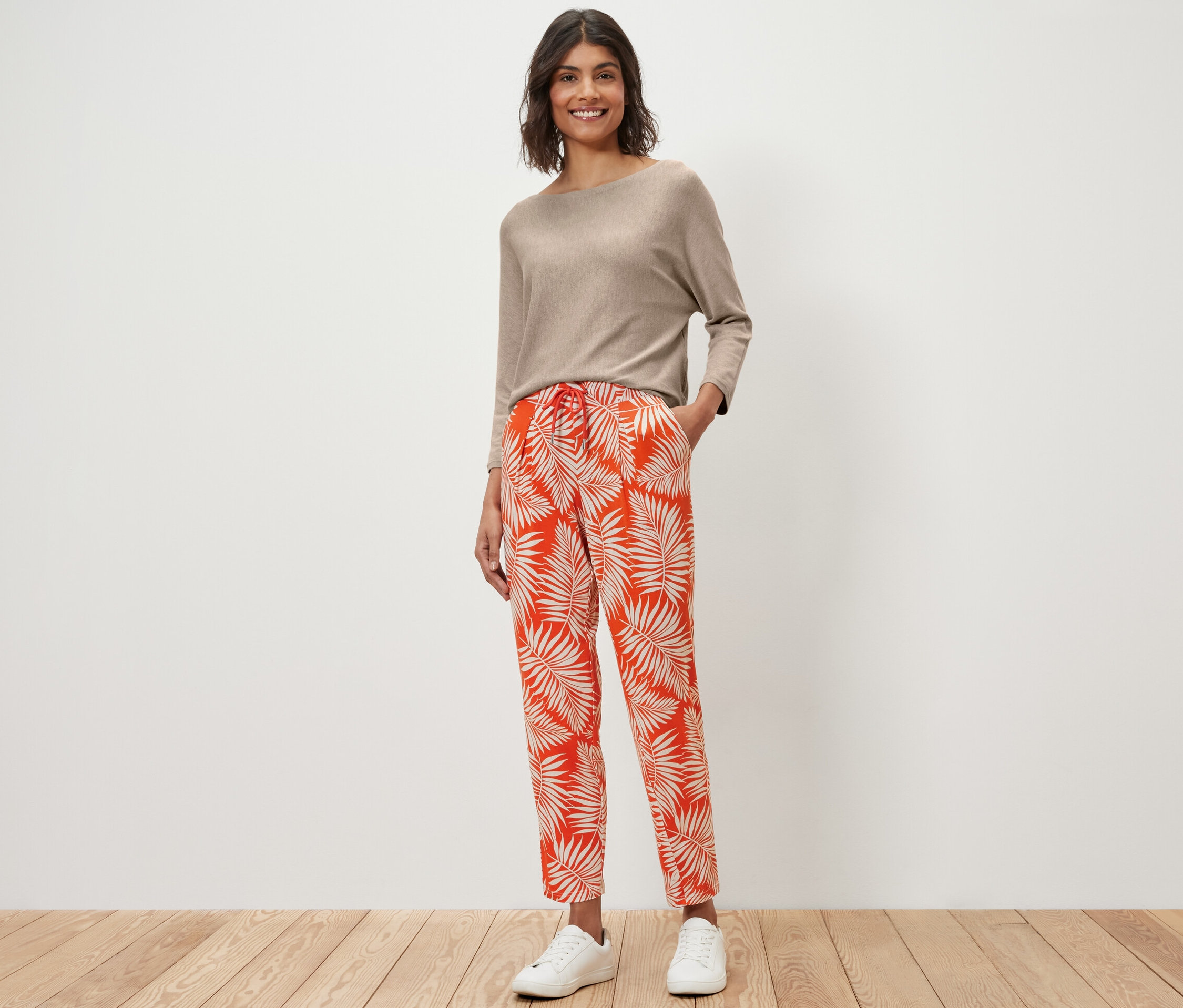 Kadın bej rengi bir üst ve baskılı jarse pantolon giyiyor, ayakta duruyor