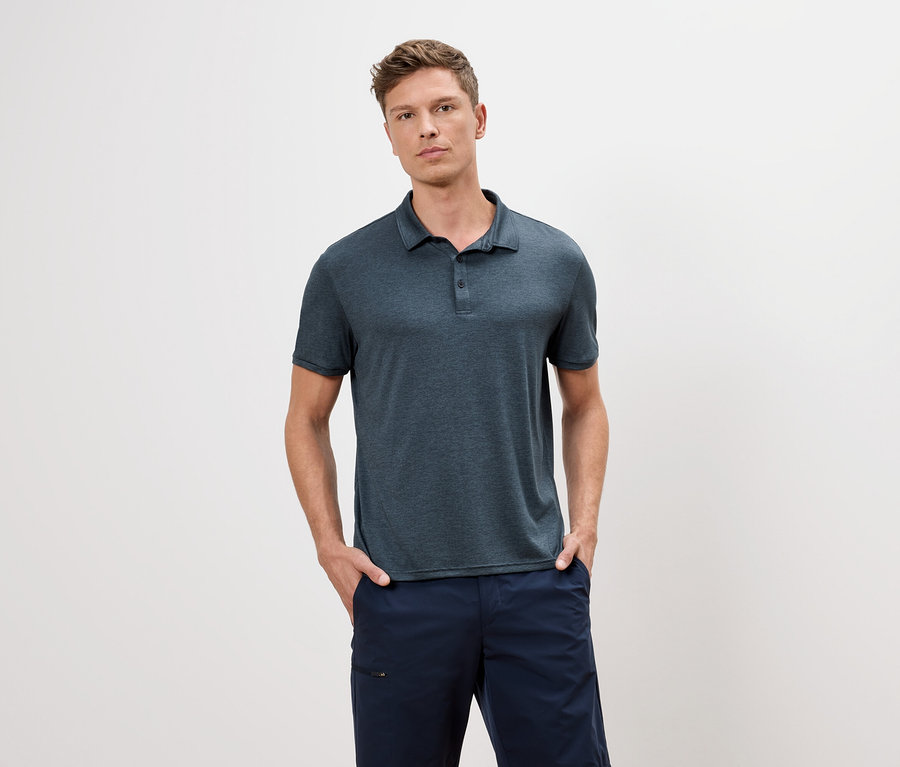 Mavi polo tişört ve mavi şortlu bir adam beyaz bir arka planda duruyor.