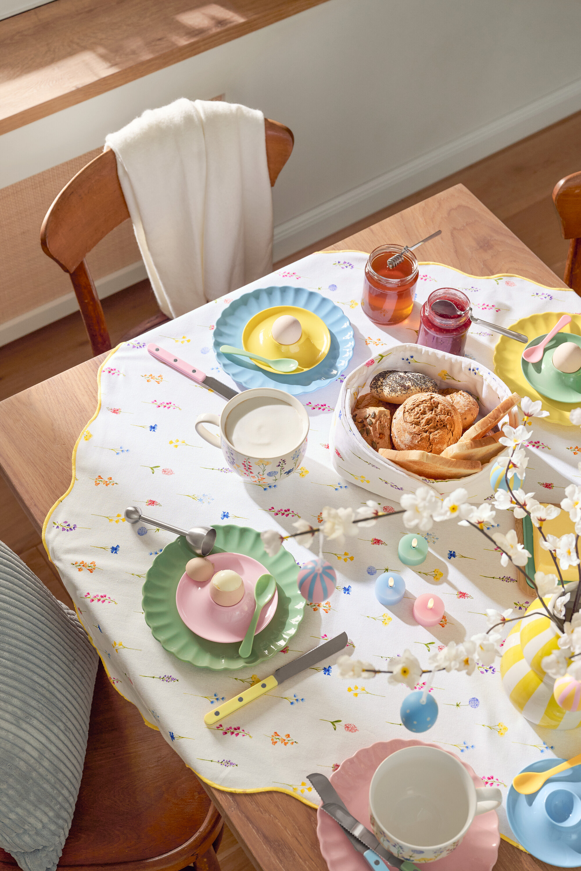 Yemek masası; tabaklar, yumurtalar, kupalar, çatal bıçak takımı, ekmek sepeti, reçel kavanozları, Paskalya süslemeleri ve çiçekli bir masa örtüsü dahil olmak üzere sofra takımı ile birlikte.