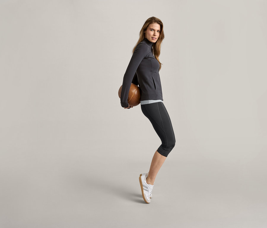 Kadın sırtında kahverengi bir top tutuyor, gri bir ceket ve siyah/gri 2 Adet Atlet giyiyor.