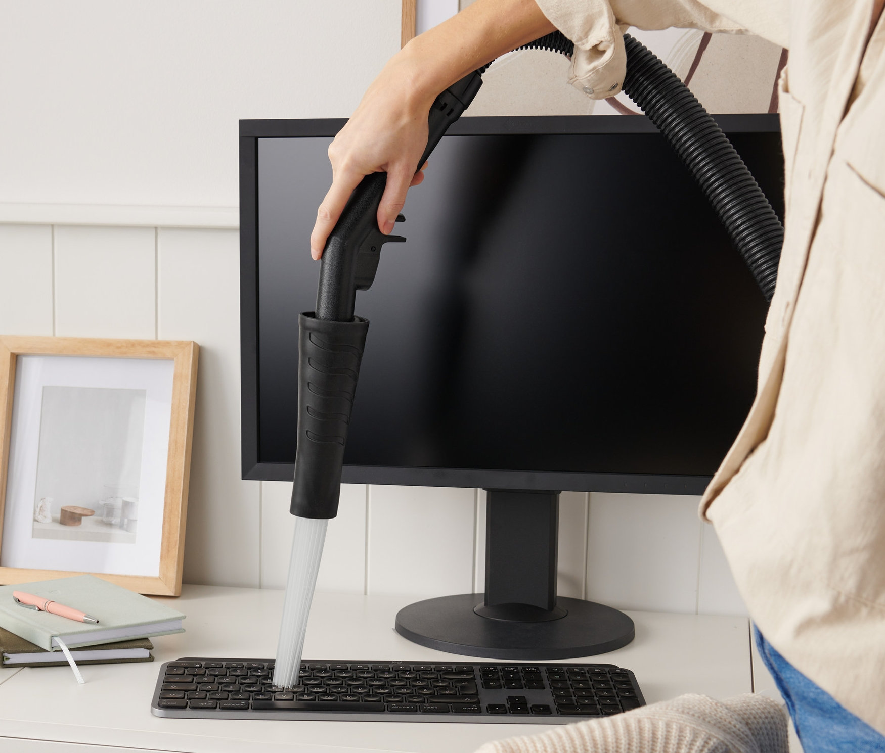 Kadın bir masanın üzerindeki klavyeyi elektrikli süpürge başlığıyla temizliyor.