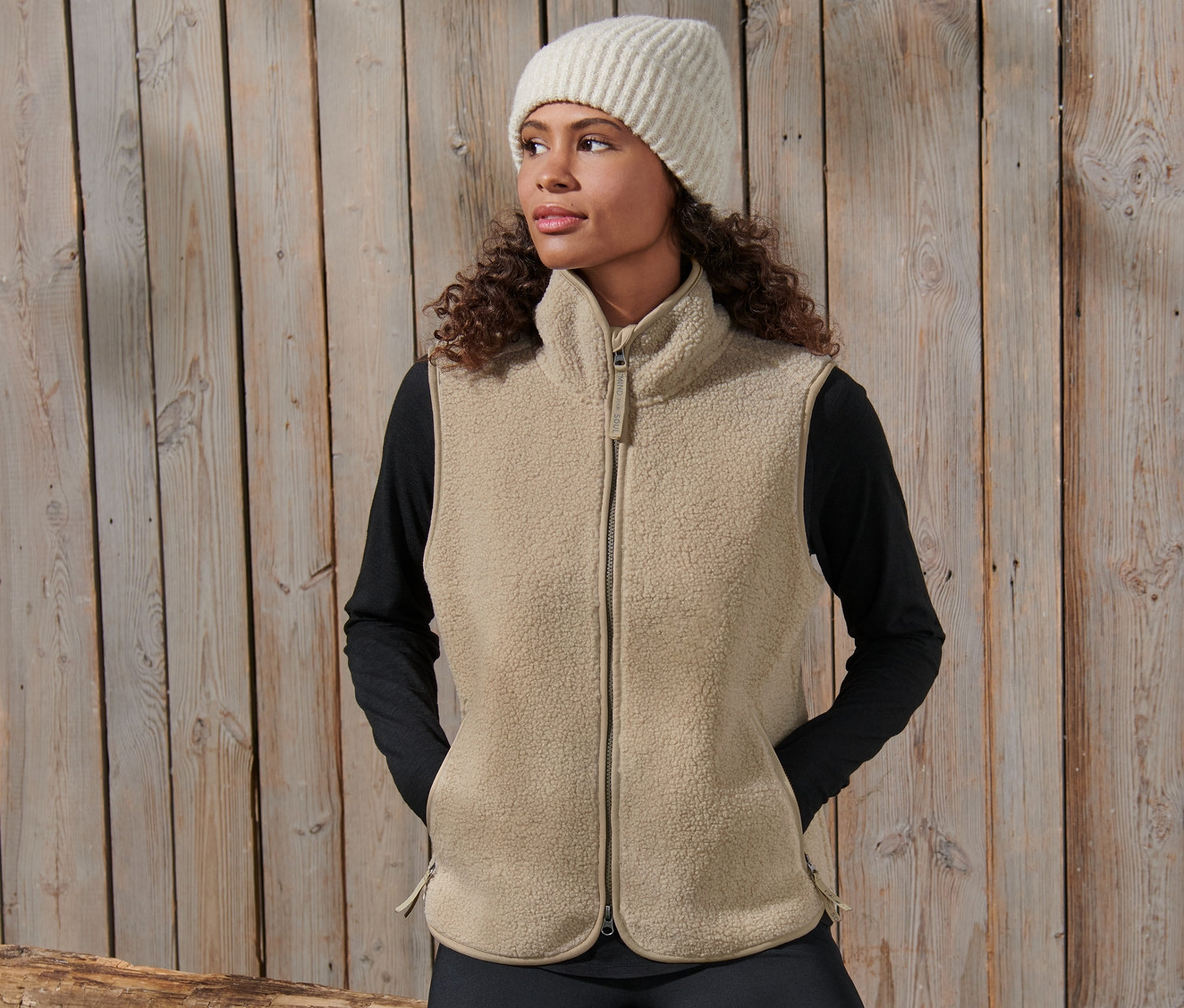 Kadın pelüş yelek ve yün şapka ile poz veriyor.