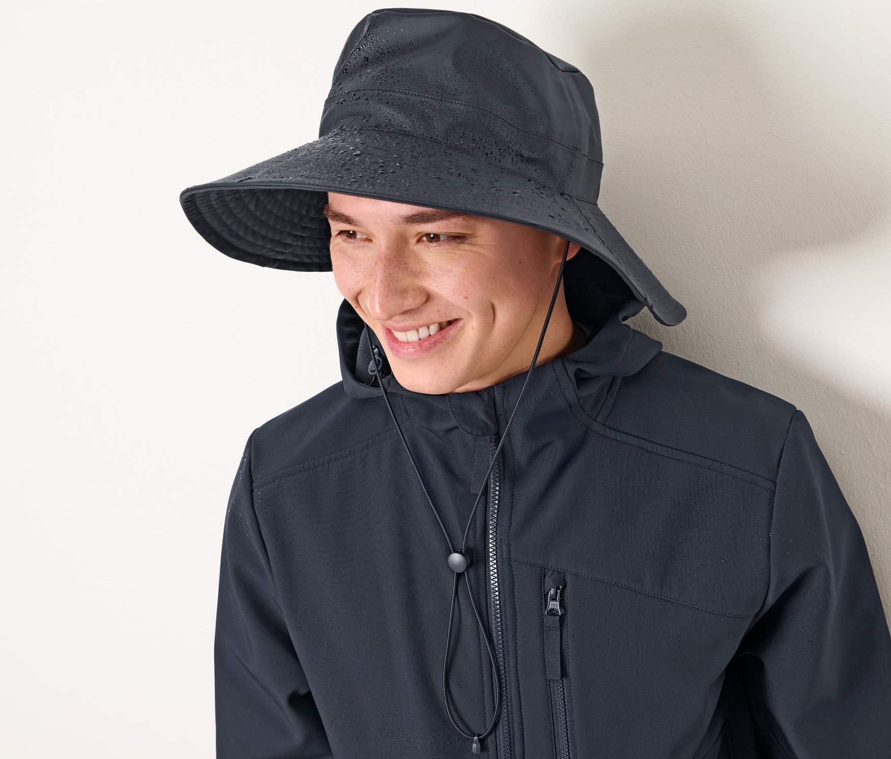 Adam lacivert yağmur şapkası ve ceket giyiyor, gülümsüyor.