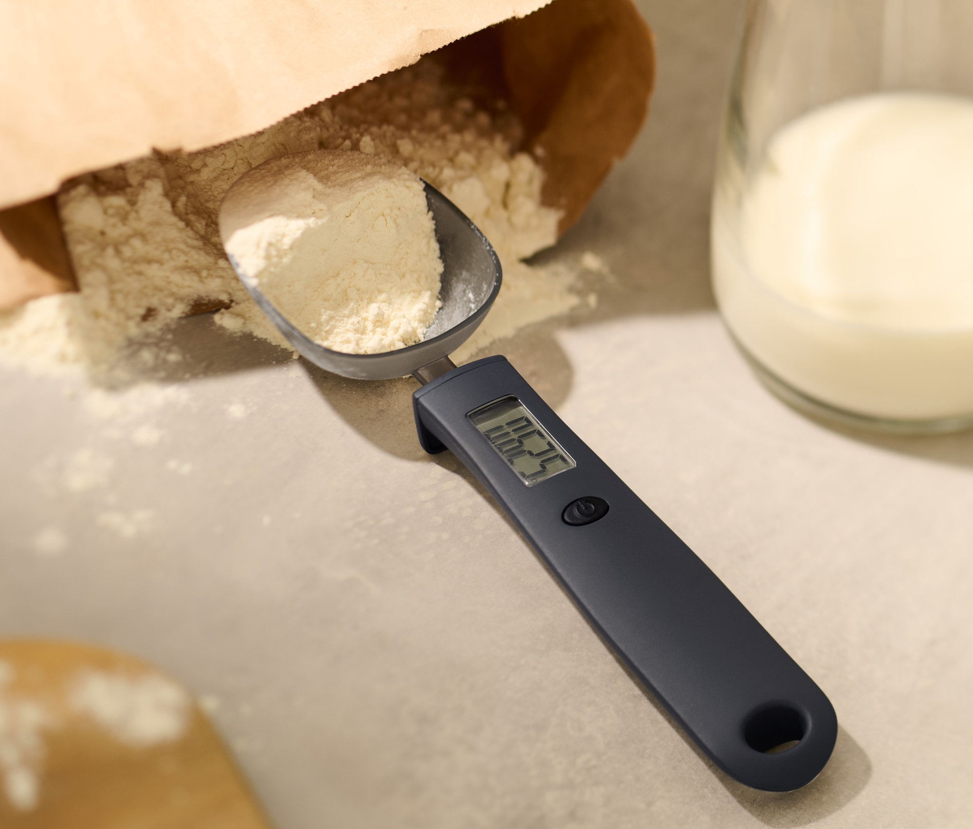 Dijital kaşık tartıda un, yanında bir bardak süt.
