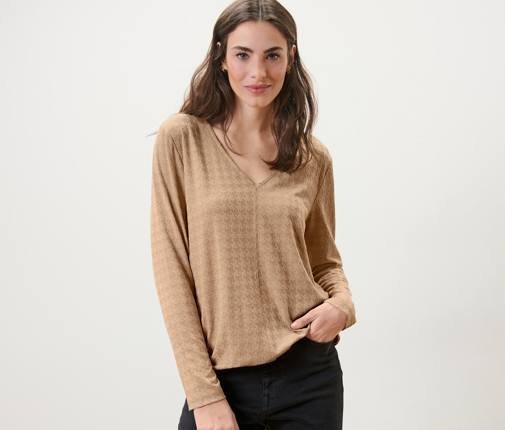 Kadın deve tüyü rengi dokulu uzun kollu gömlekle poz veriyor.