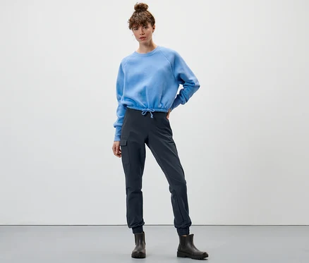 Kadın mavi bir sweatshirt ve lacivert softshell jogger pantolonla poz veriyor.