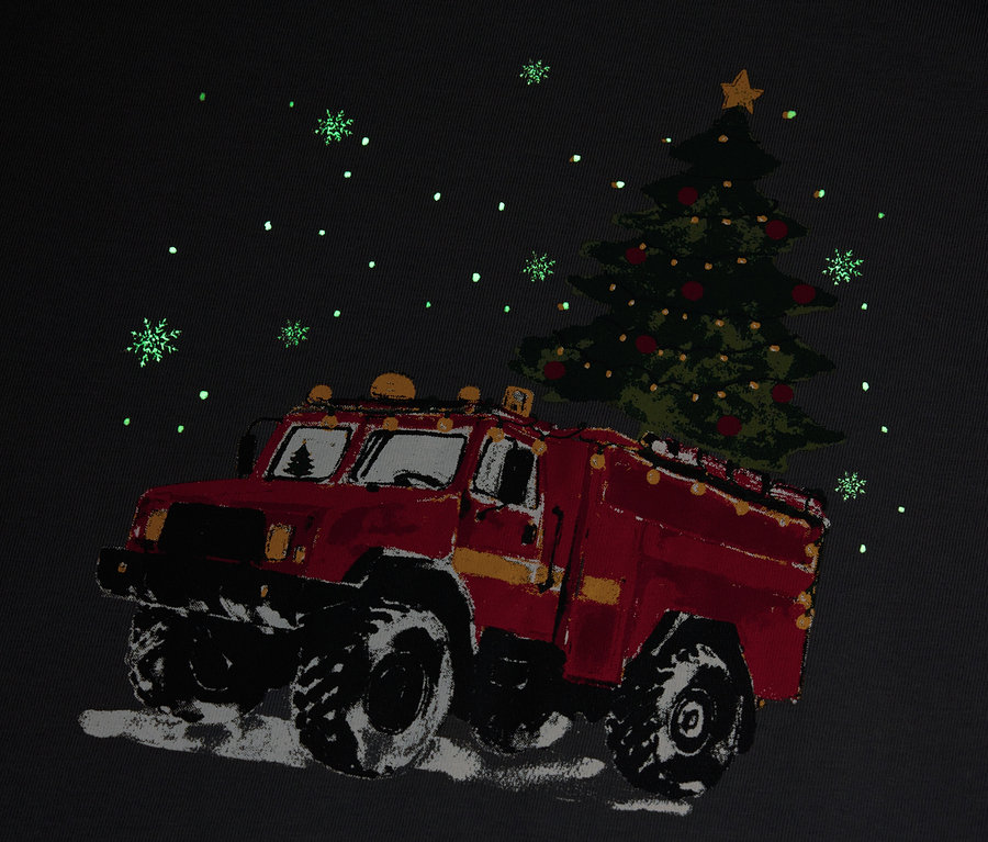 Kırmızı bir itfaiye aracı kar yağışı altında bir Noel ağacı taşıyor.