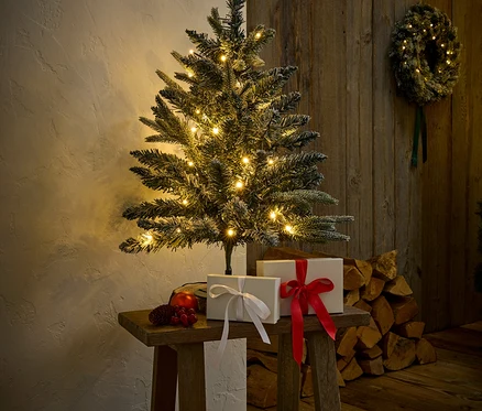 Ahşap bir tabure üzerinde ışıklı bir Noel ağacı, hediyeler ve süslemelerle birlikte duruyor.