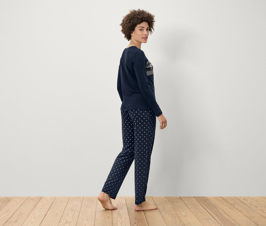 Kadın, beyaz puantiyeli lacivert pijamayla ahşap zeminde yürüyor.