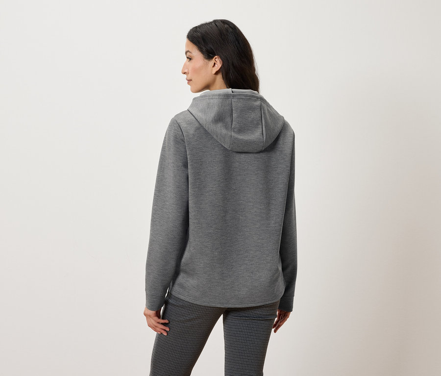 Gri kapüşonlu sweatshirt ve desenli pantolon giyen bir kadının arka görünümü.