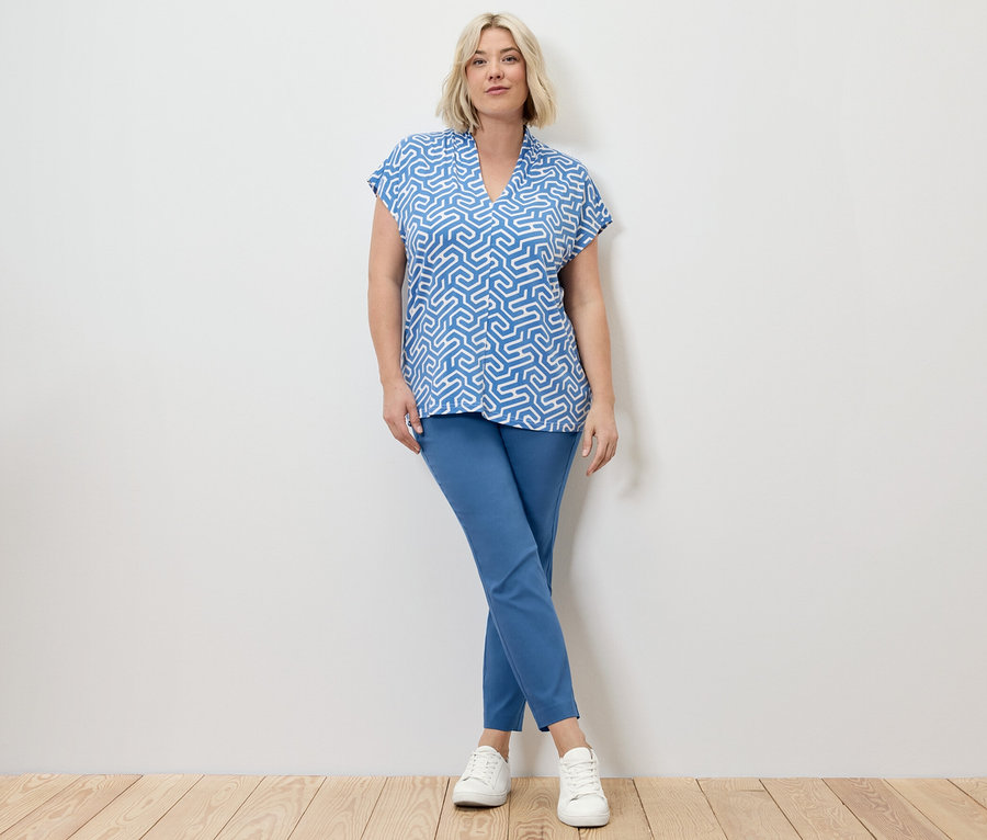 Sarışın bir kadın mavi streç pantolon ve V yakalı mavi bluzla poz veriyor.