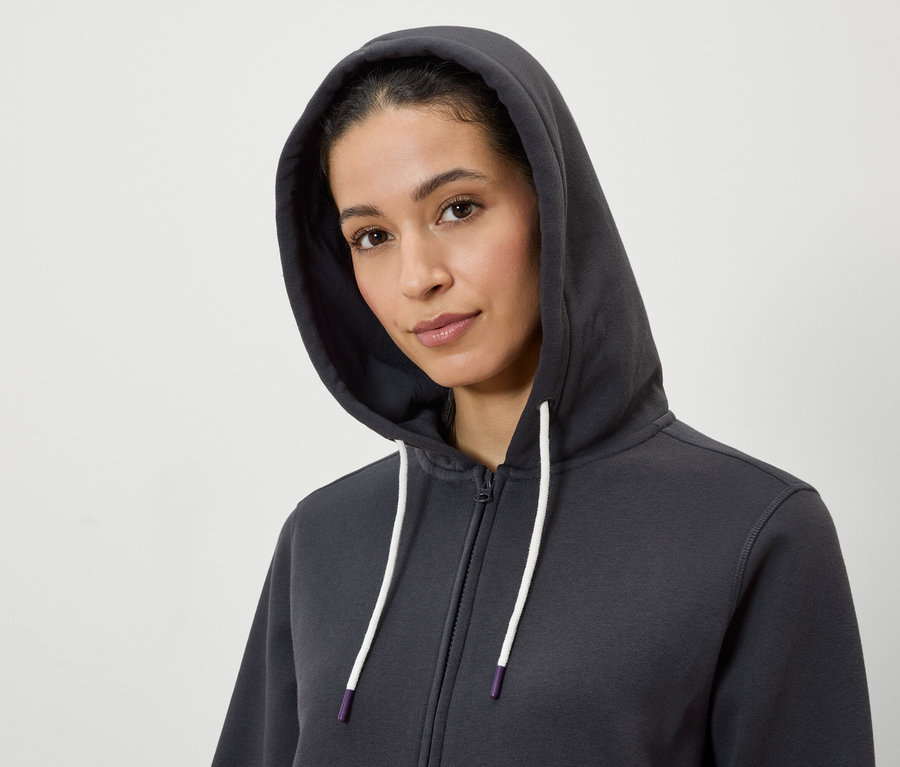 Kapüşonlu, gri, fermuarlı ve beyaz ipli bir sweatshirt giyen bir kadının portresi.