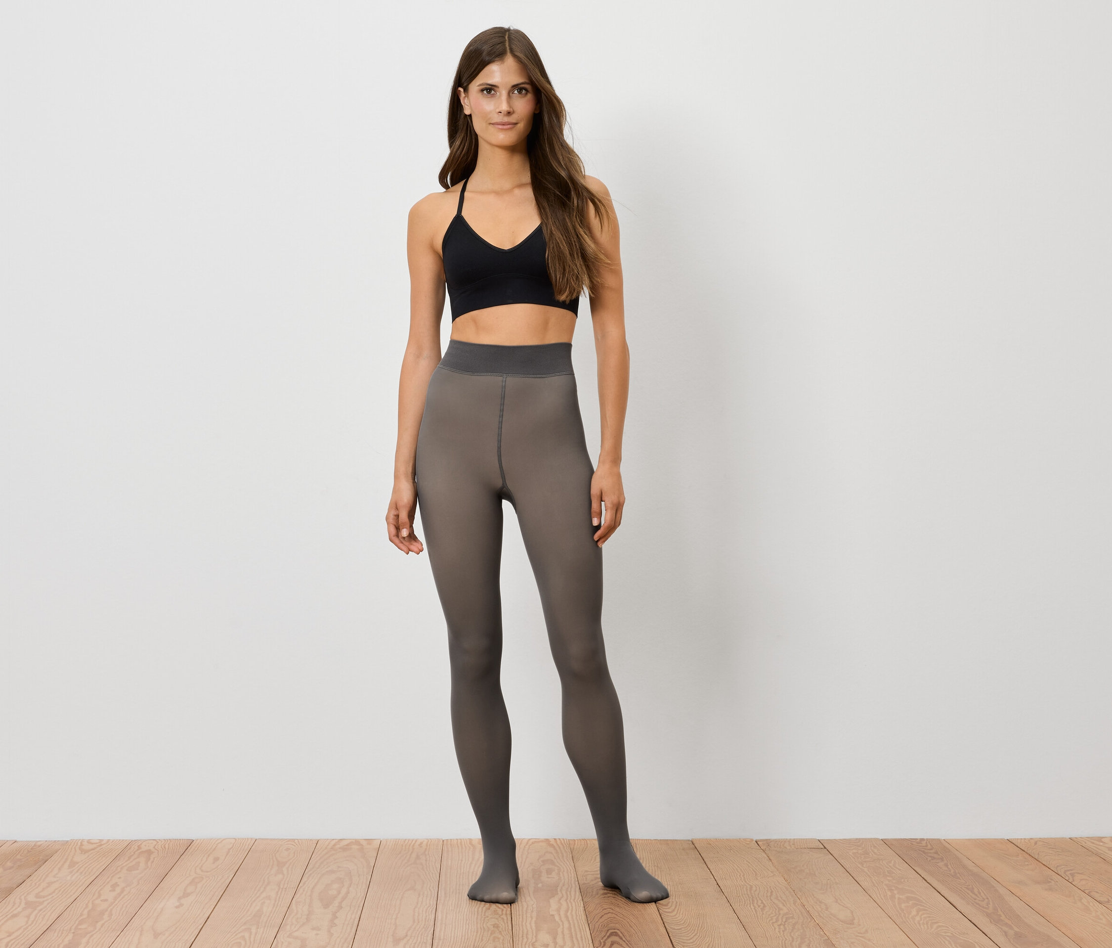 Kadın ayakta duruyor, üzerinde siyah bir sporcu atleti ve gri külotlu çorap var.