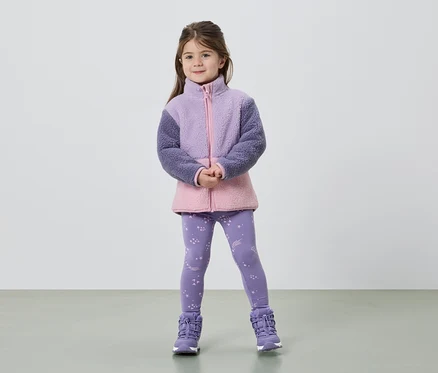 Elleri birleşik duran bir kız, mor ve pembe renklerde bir polar ceket, yıldız desenli tayt ve mor botlar giyiyor.