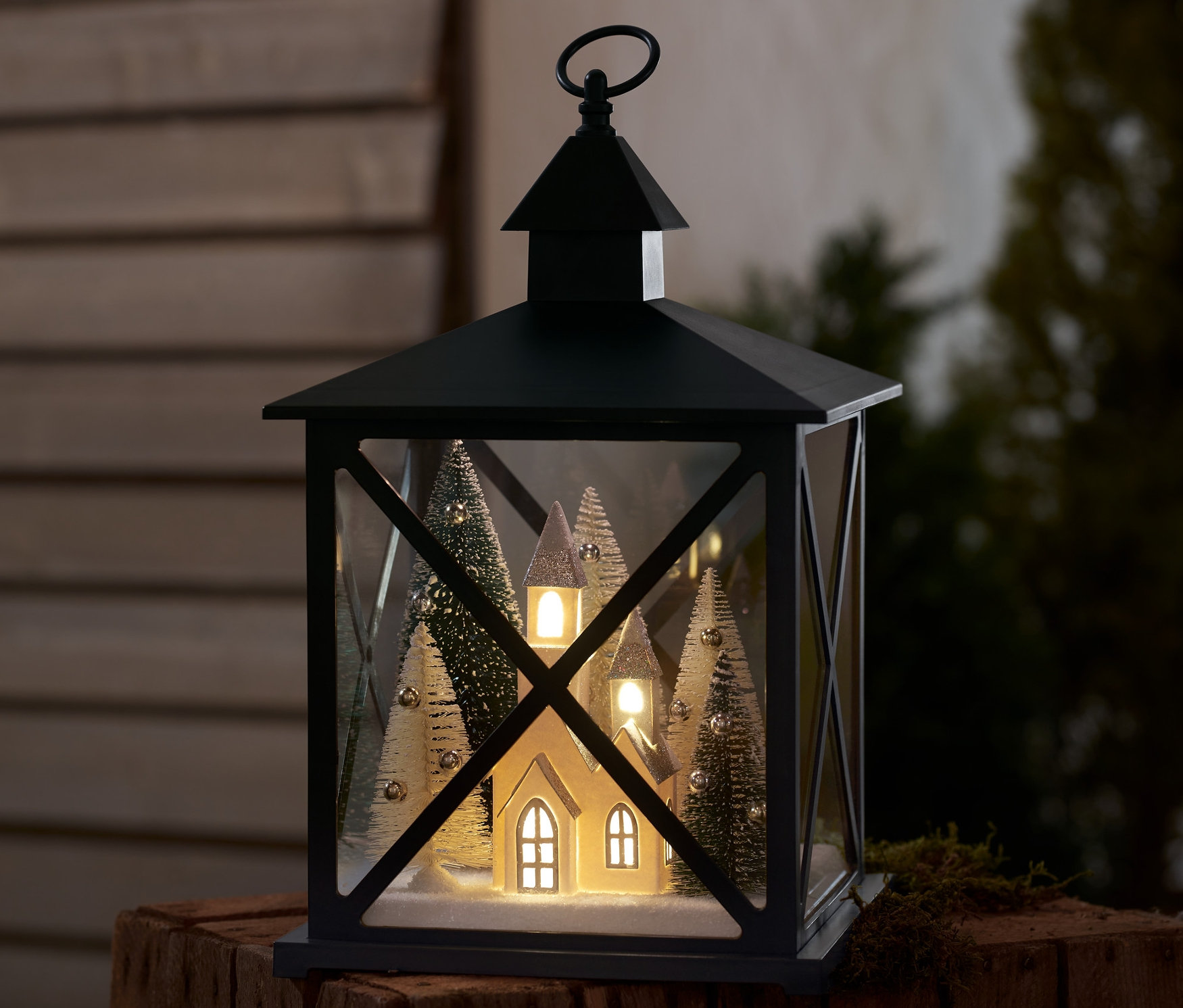 Kış ormanı temalı bir LED dekoratif fener ahşap bir yüzey üzerinde duruyor.