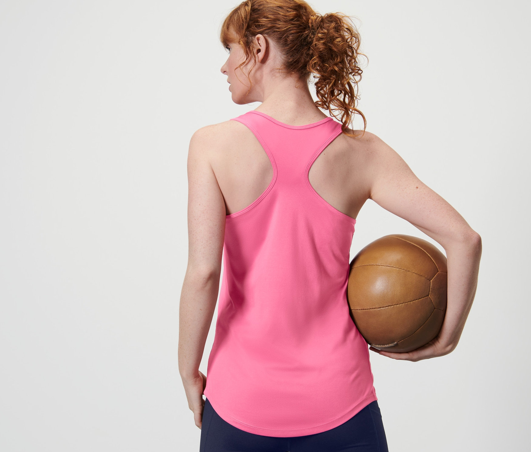 Arkadan görünüşüyle bir kadın kahverengi bir top tutuyor ve 2'li setten pembe bir atlet giyiyor.