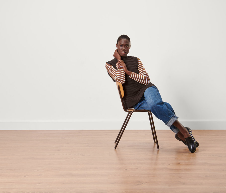 Kadın sandalyede oturuyor ve Örgü Süveter giyiyor.