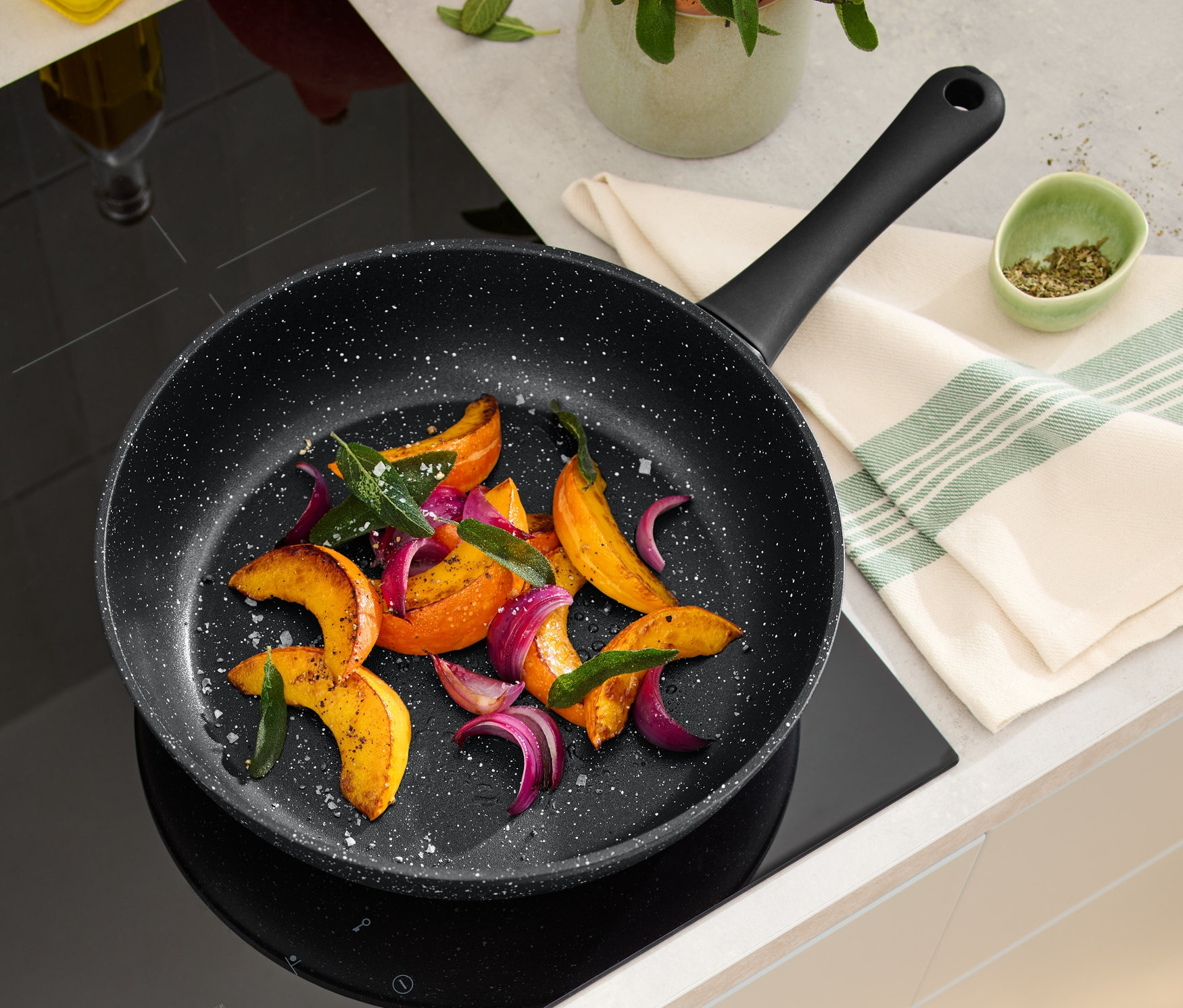 İndüksiyonlu ocakta kızarmış sebzelerle dolu 28 cm'lik taş görünümlü profesyonel bir tava duruyor.