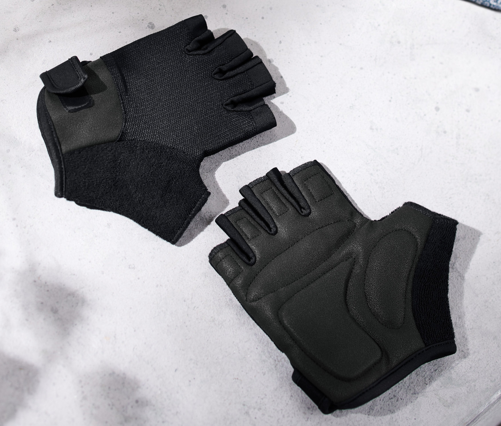 Gri bir bankta, mavi bir havlunun yanında duran iki adet siyah fitness eldiveni.