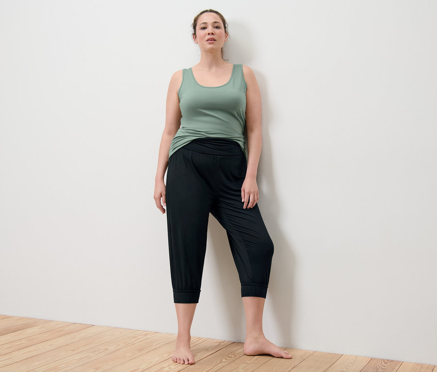 Kadın yeşil atlet ve siyah 3/4 yoga pantolonuyla poz veriyor.