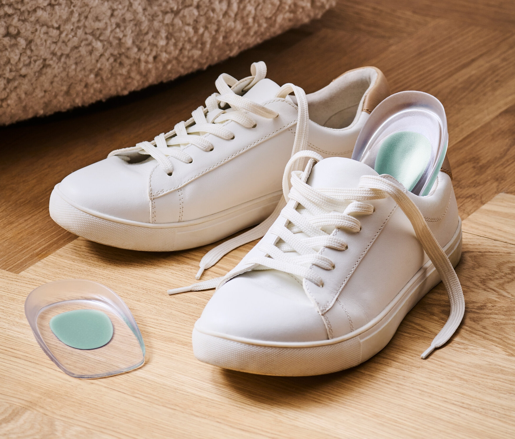 Ahşap bir zeminde iki beyaz spor ayakkabı ve 1 Çift Topuk Desteği.
