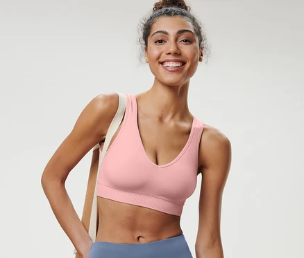 Gülümseyen bir kadın pembe dikişsiz spor büstiyer giyiyor.