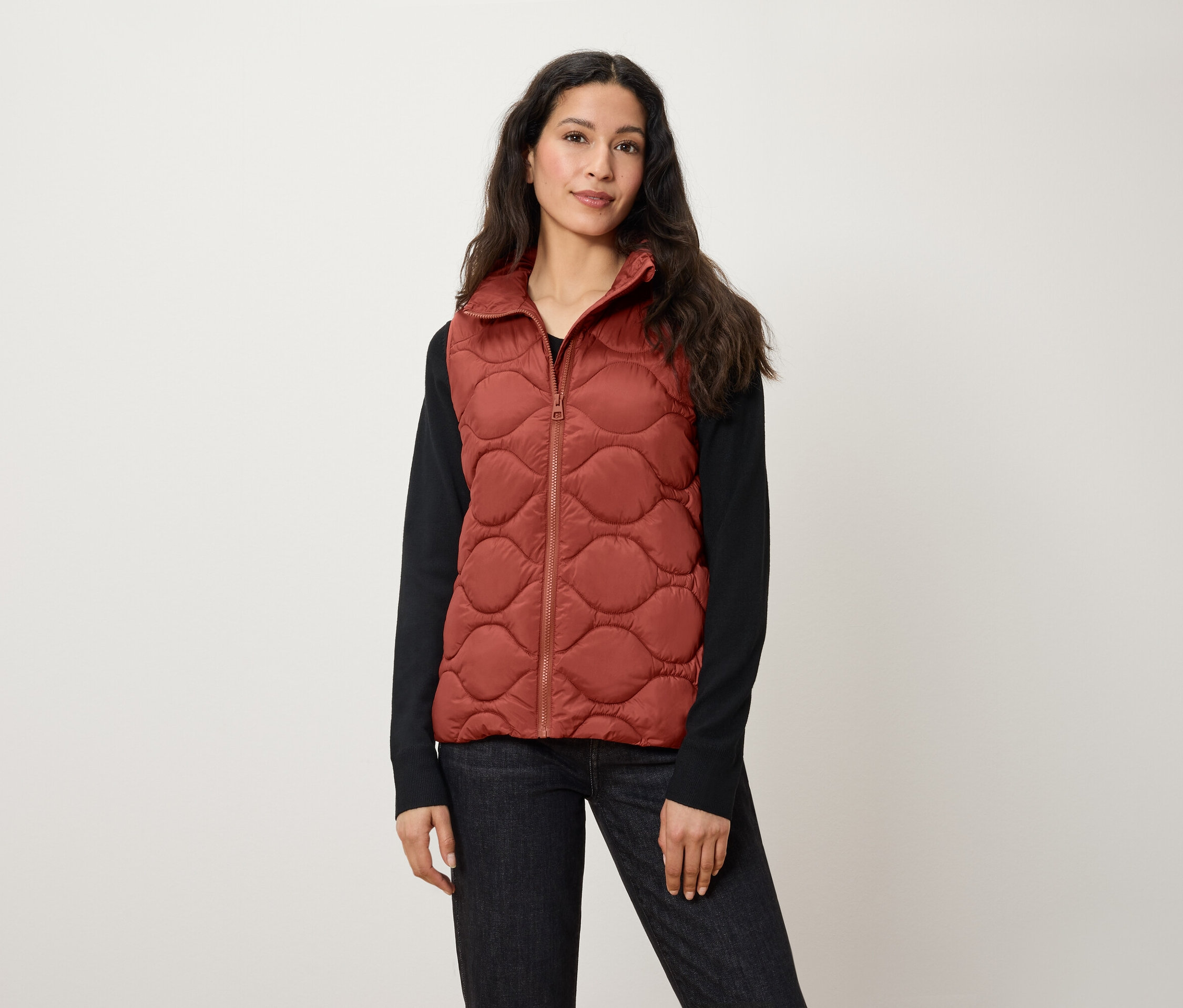 Kadın pas rengi kapitone yelek giyiyor.