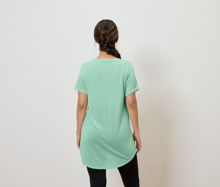 Sırtı kameraya dönük bir kadın, yeşil bir tişört ve siyah tayt giyiyor.