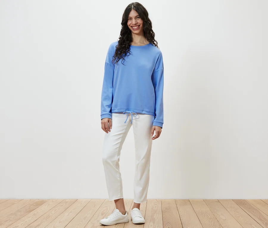 Kadın ayakta duruyor ve açık mavi bir sweatshirt giyiyor.