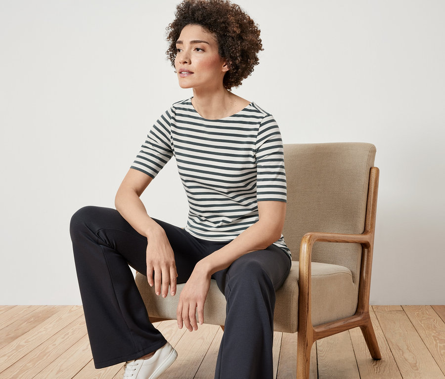 Kadın sandalyede oturuyor ve yeşil çizgili, yarım kollu bir tişört giyiyor.