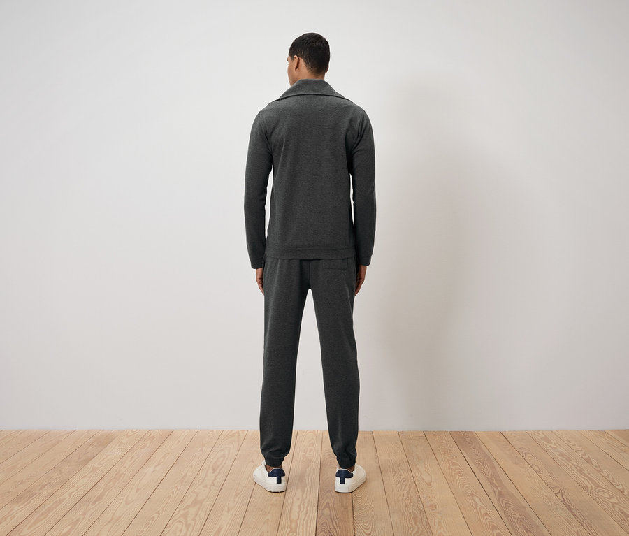 Arkası kameraya dönük, koyu gri eşofman ve beyaz spor ayakkabı giyen adam.