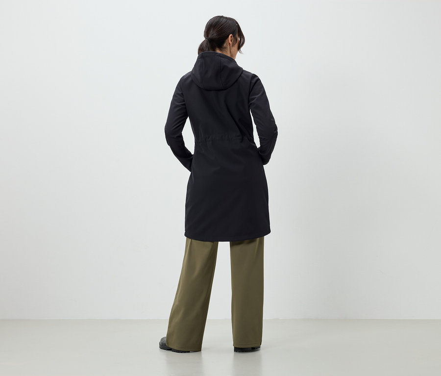 Sırtı kameraya dönük bir kadın, siyah bir manto ve yeşil pantolon giyiyor.